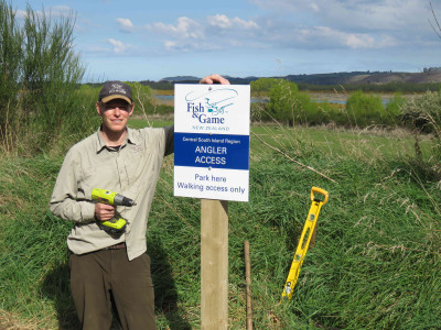Photo 3 Fish Game Officer Rhys Adams with a newly installed angler access sign on the Waitaki River at Stone wall